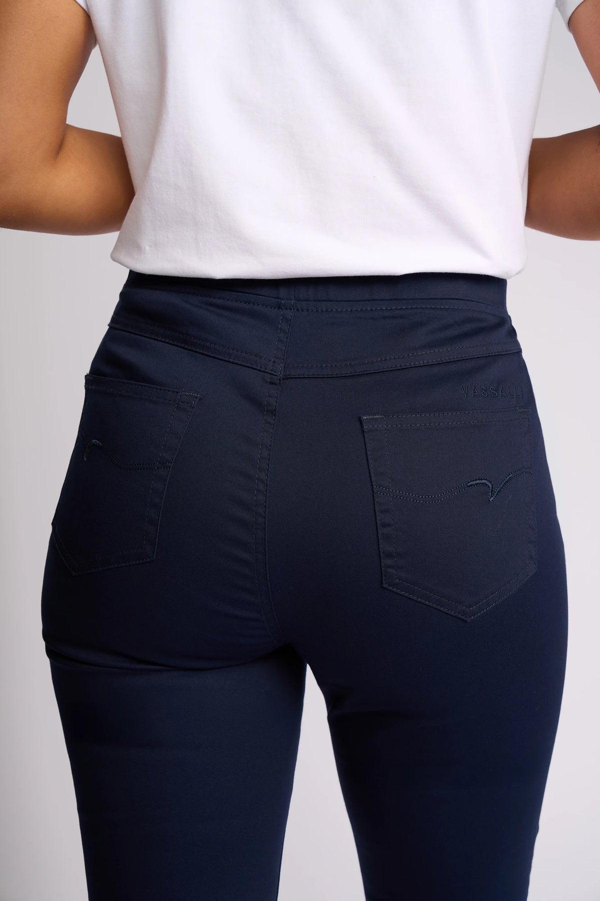 A person is shown from the back wearing the Vassalli Sierra 7/8 Pant in Navy with a white shirt, highlighting the pants’ pockets and seam details against a neutral background.