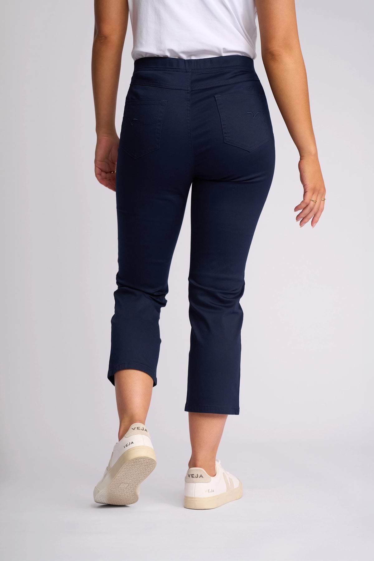 A person wearing a white t-shirt, the Vassalli Sierra 7/8 Pant in Navy, and white Veja sneakers stands facing away on a plain background.
