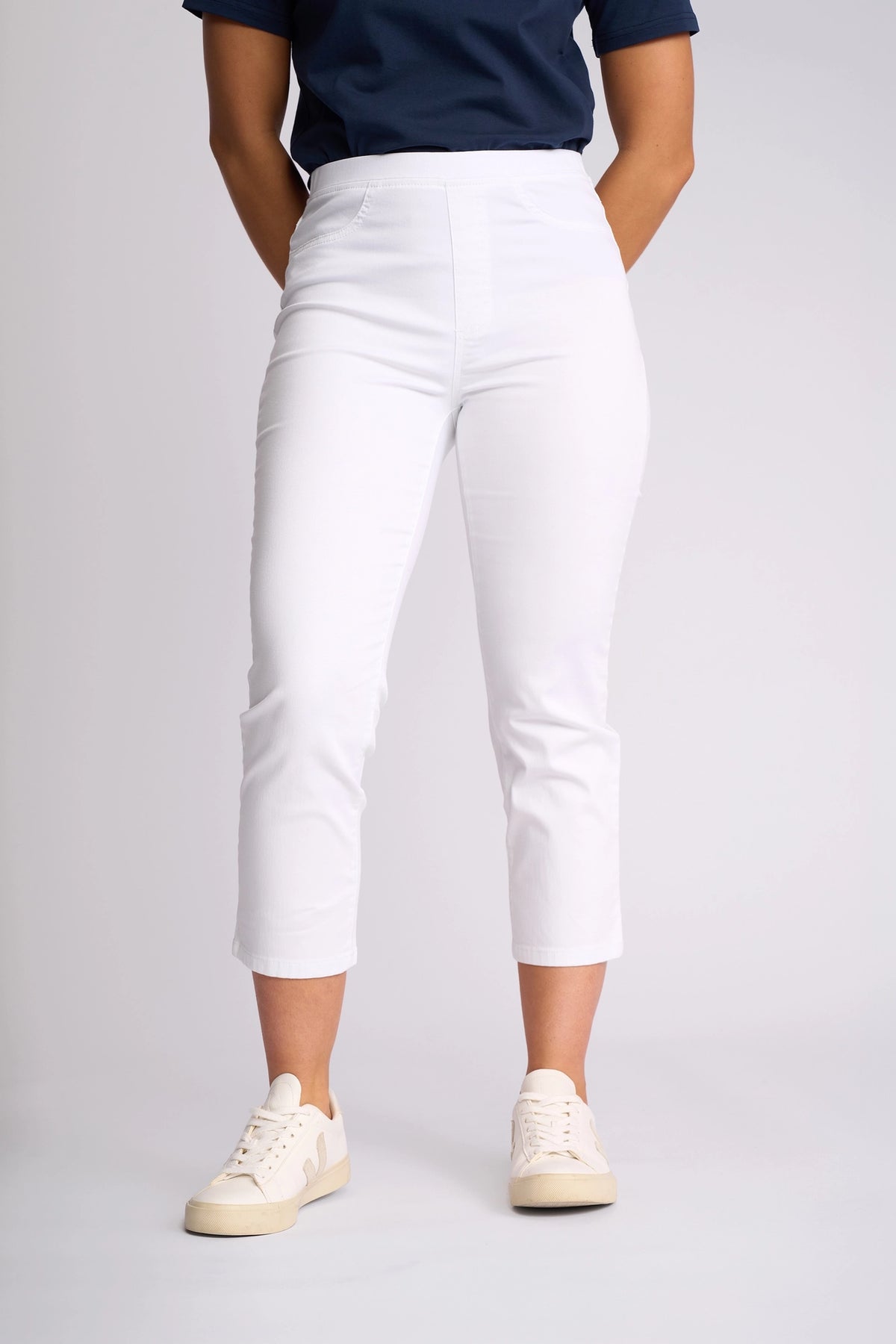A person wearing a navy blue shirt, Vassalli Sierra 7/8 Pant in White, and beige sneakers stands against a plain light background.