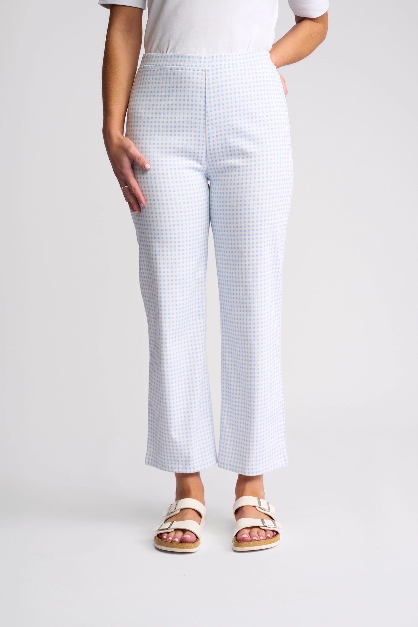 A person wearing white heeled sandals, a white top, and the Vassalli Seattle Pull On pants in blue gingham, standing against a plain gray background. The photo is cropped from the shoulders down.
