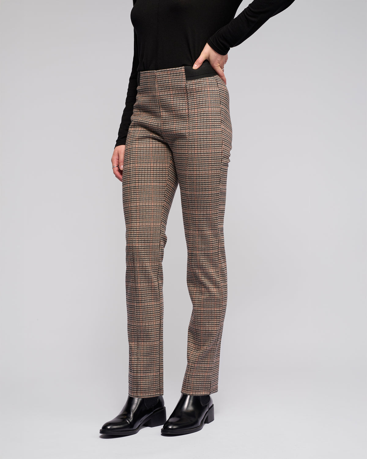 Someone models Vassalli's Everest Pull On - Ezra high-waisted, straight-leg print pants in stretch knit fabric with a black long-sleeve top and black ankle boots, standing against a plain light gray background. The person's head is not visible.