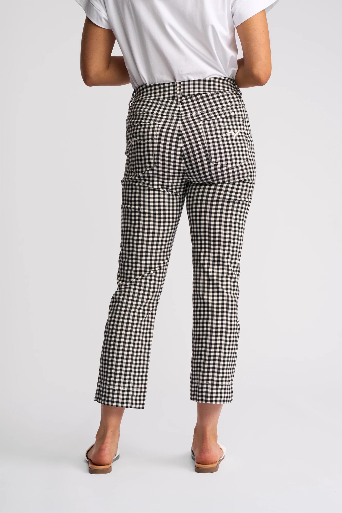 A person wearing the Vassalli Tint Pull On pants in black gingham, paired with a white short-sleeve shirt and open-toe sandals, stands with their back to the camera against a plain background.