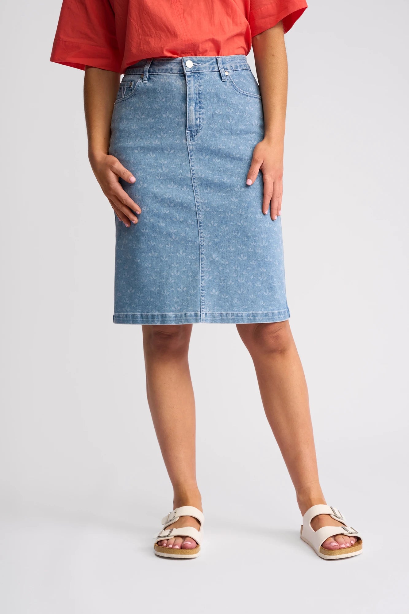 A person is wearing a red top, the Vassalli Poppy Skirt - Meadow Denim, and white sandals, standing against a plain background.