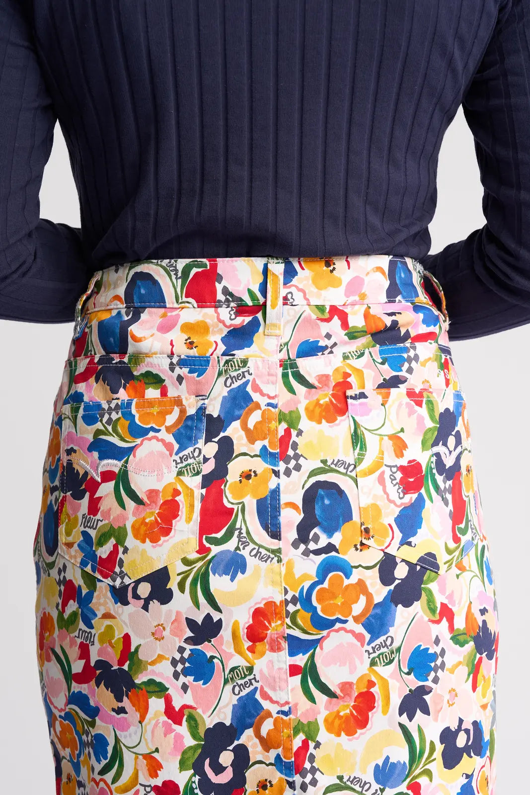 A person wearing a navy ribbed top and the Vassalli Poppy Skirt - Mon Cheri, a high-waisted floral print skirt with a colorful pattern, shown from the back.