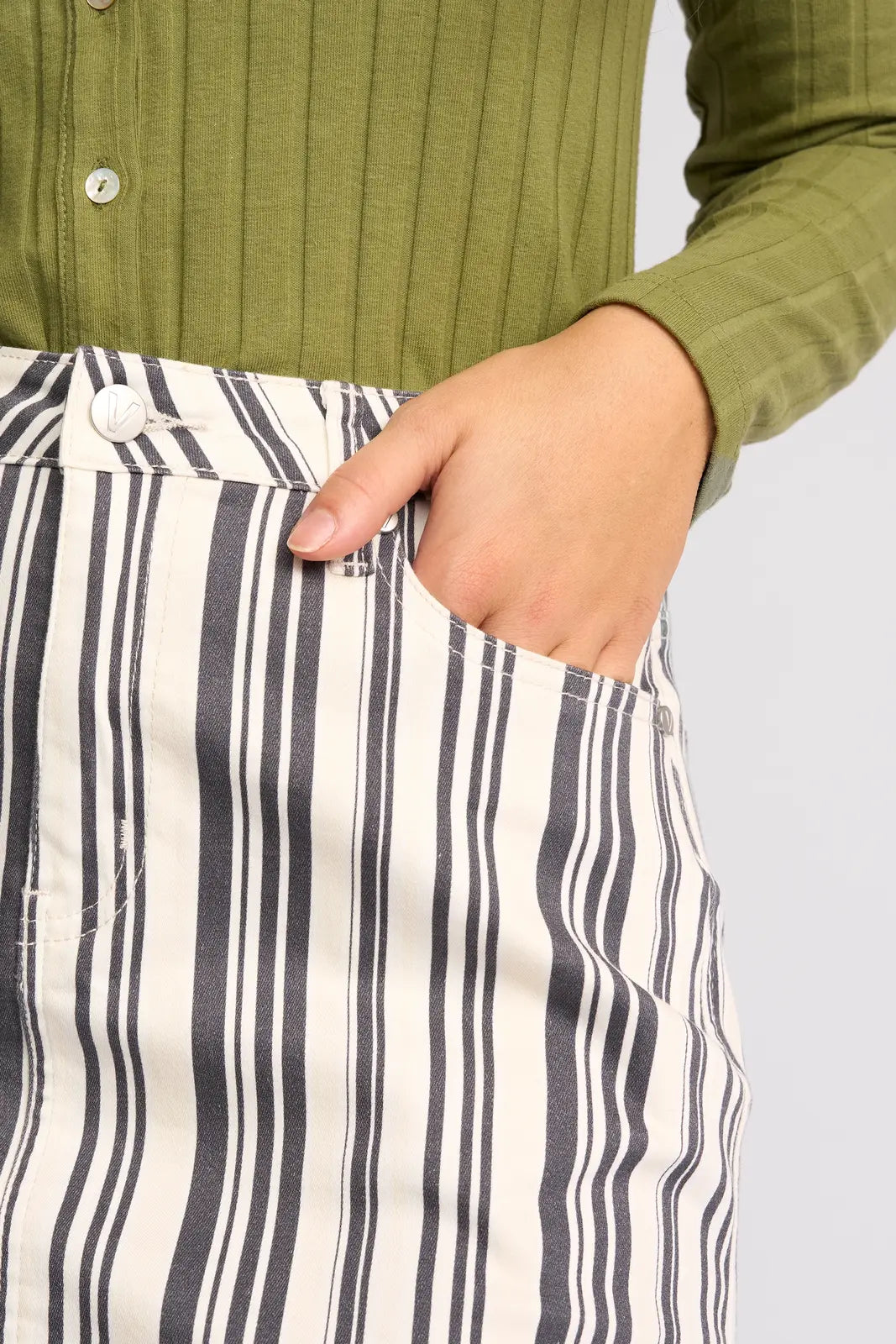 A person wearing a green ribbed shirt and the Vassalli Poppy Skirt - Multi Stripe Denim has their right hand in their skirt pocket.