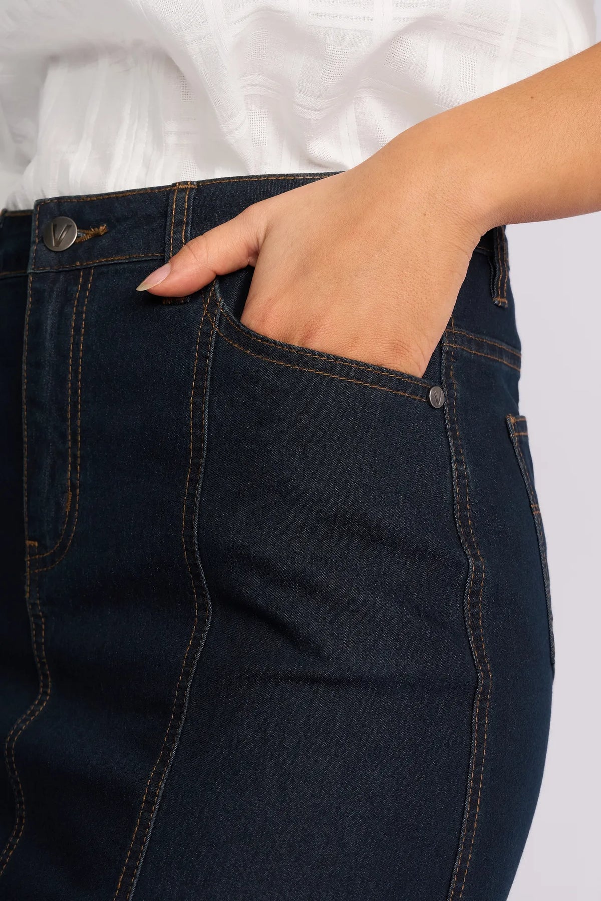 Wearing the Vassalli Poppy Skirt in Indigo Denim, a person stands with one hand in their pocket, showcasing the front and side stitching details of the skirt.