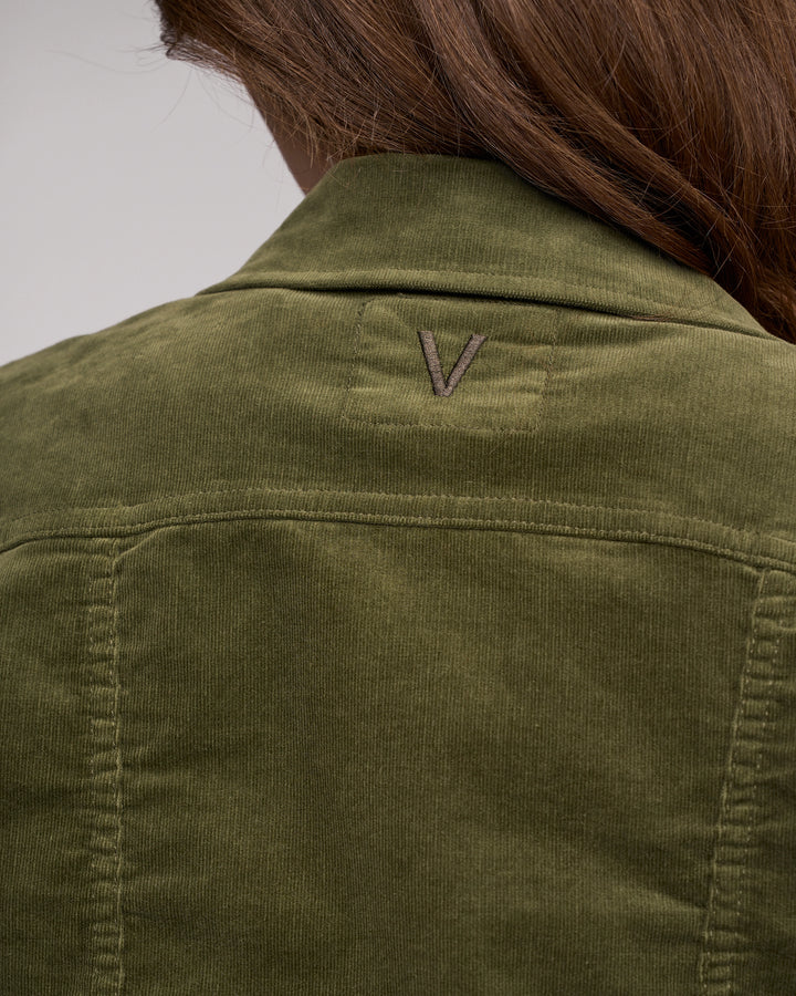 A close-up of the back of a person wearing the Vassalli Core Cord Jacket - Deep Sage, styled like a denim jacket with brown hair visible and a stitched V logo on the upper back.