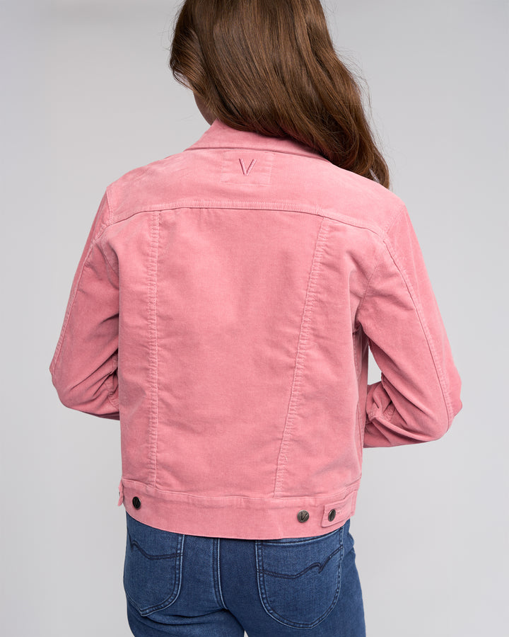 A person with long brown hair is seen from behind, wearing the Vassalli Core Cord Jacket in dusky pink and blue jeans, standing against a plain light gray background.
