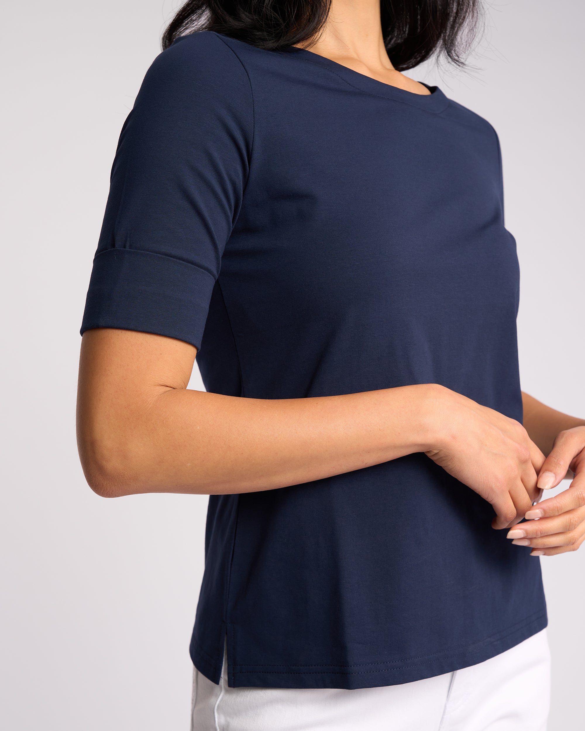 A woman wears the Vassalli Arden Top - Navy with white pants, standing against a plain light background with her hands loosely clasped near her waist.