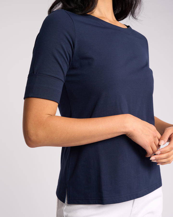 A woman wears the Vassalli Arden Top - Navy with white pants, standing against a plain light background with her hands loosely clasped near her waist.