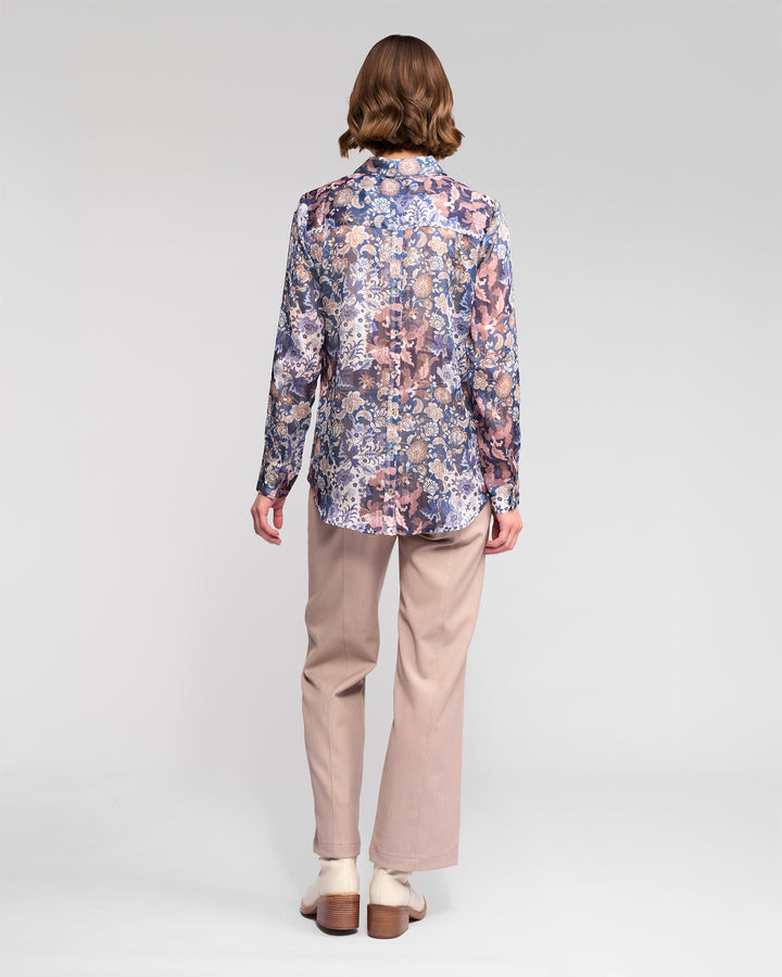 A person stands facing away, wearing the Vassalli Ballot Shirt - Rhea, paired with light beige pants and white shoes against a plain light gray background.