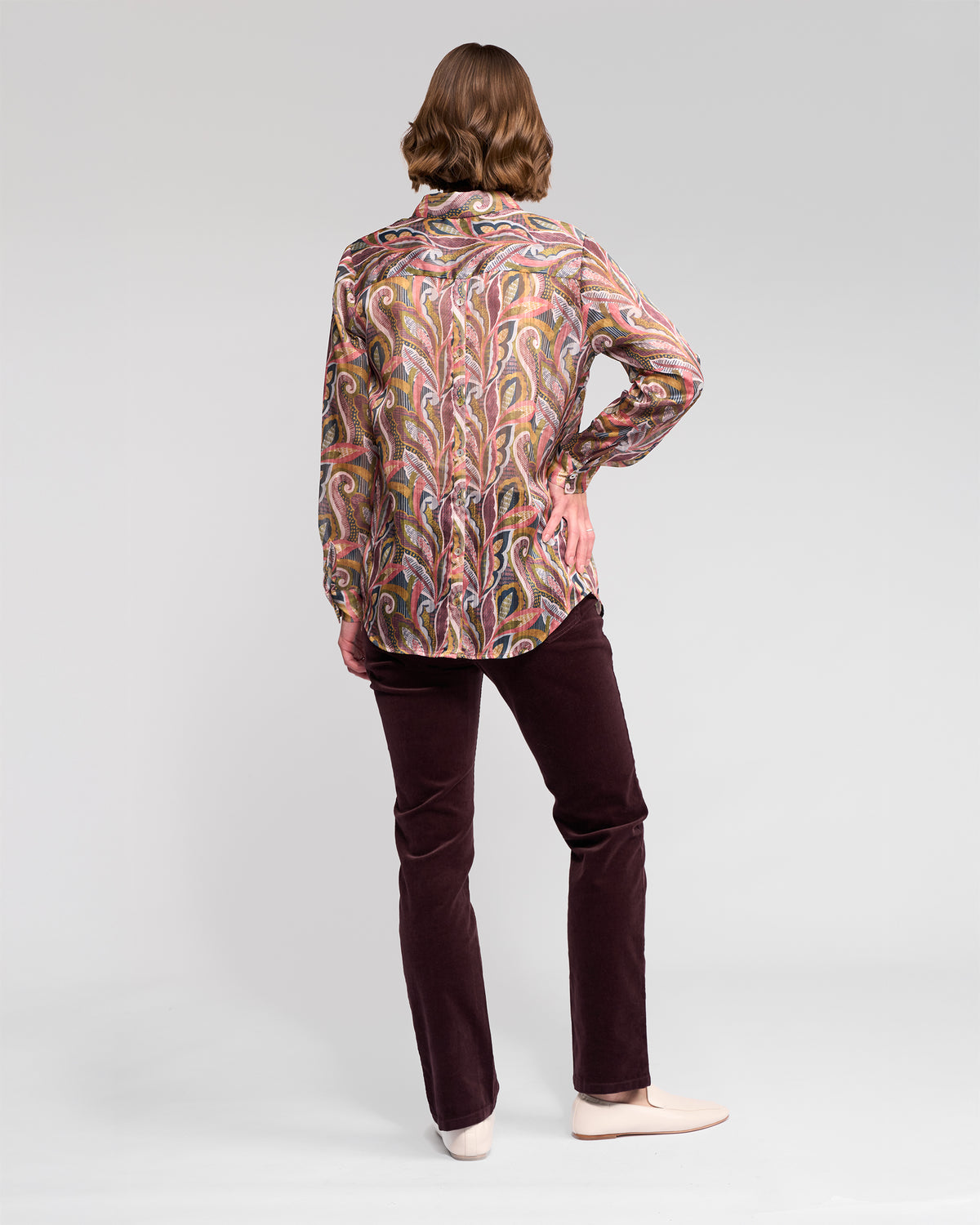 A person stands facing away, wearing the Vassalli Ballot Shirt - Sable with long sleeves, dark maroon pants, and light shoes against a plain light background.