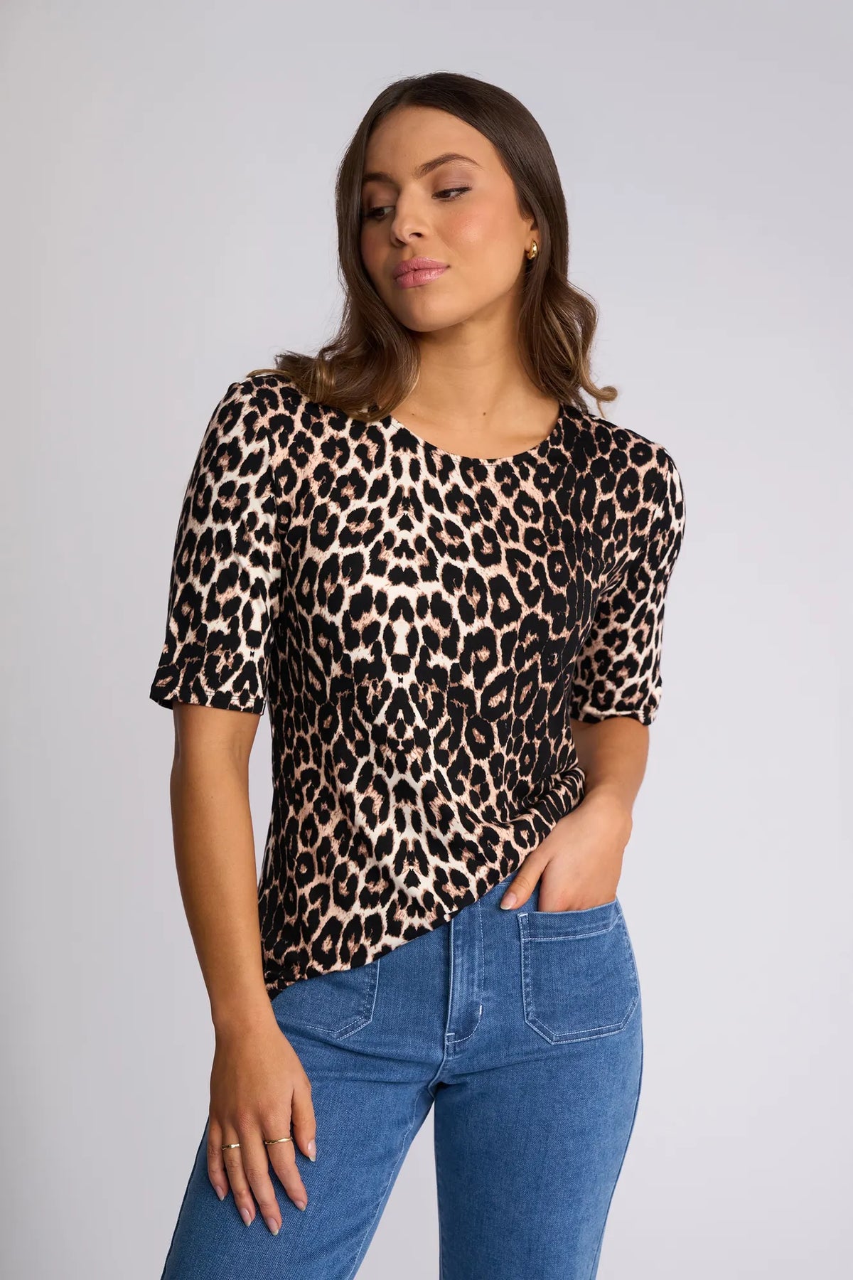 Woman wearing a short-sleeved Carmen Top - Leopard and blue denim jeans with front pockets.