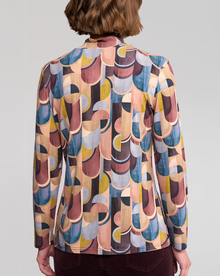 A person with short brown hair is seen from behind wearing the Vassalli Foundation Top – Revolve, a long-sleeve, high-neck stretch jersey featuring retro geometric prints in pink, yellow, blue, and brown.