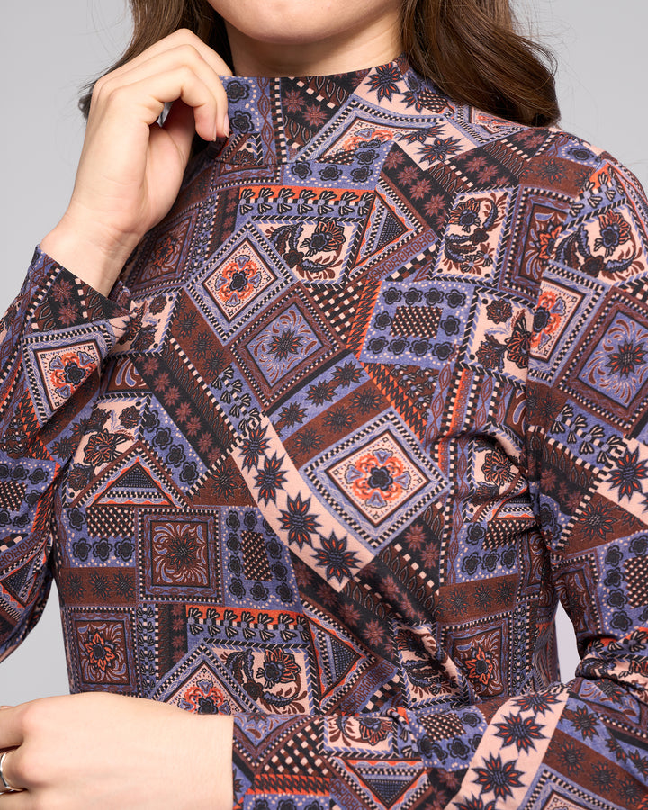 A woman wears the Vassalli Foundation Top - Rue, a long-sleeve high-neck stretch jersey with colorful geometric and floral patterns in purple, blue, red, and beige, holding the collar near her face.