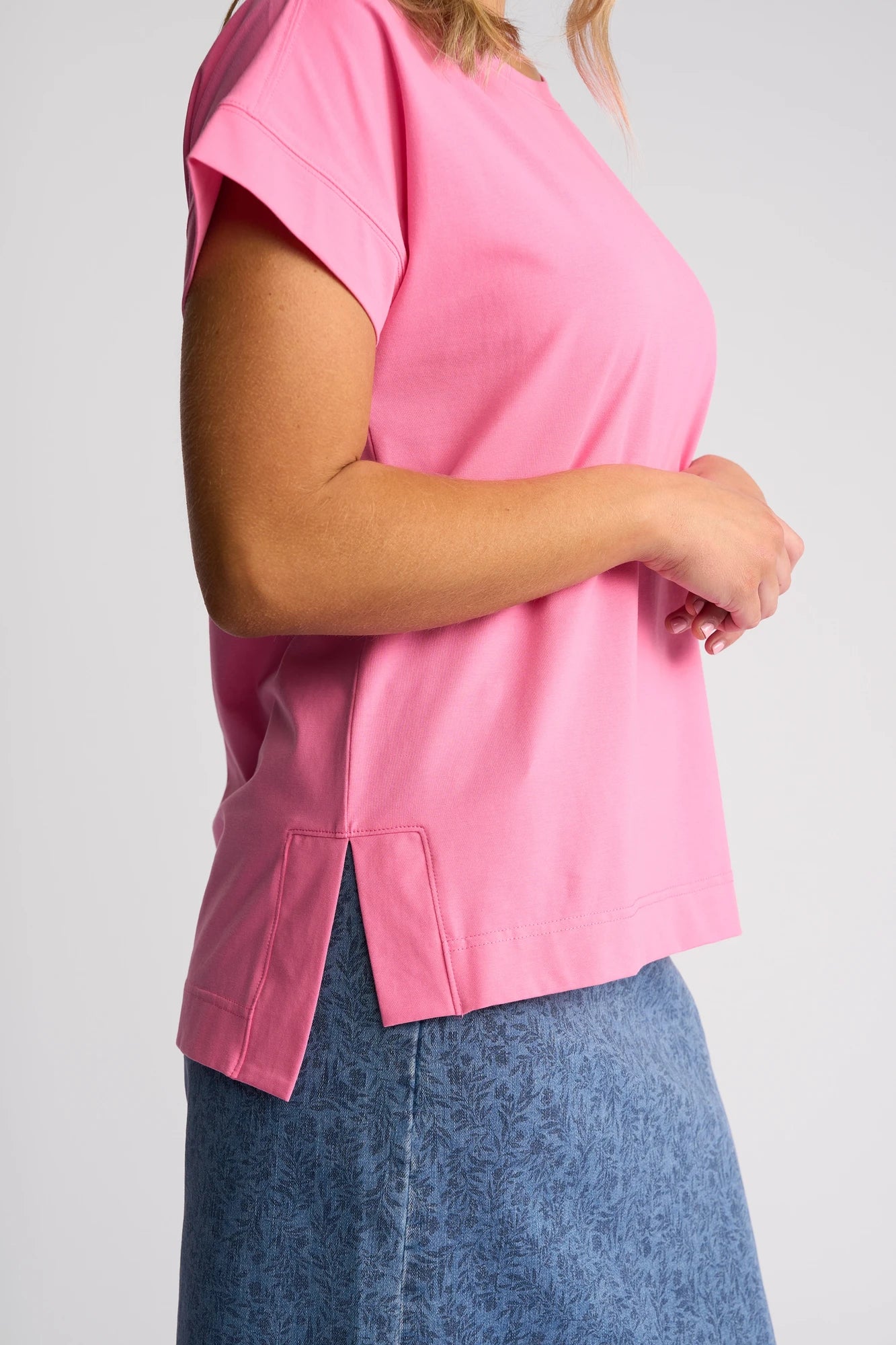A person wearing the Vassalli Thea Top in Sweet Pink and a blue patterned skirt stands against a plain background, shown from the shoulders down.