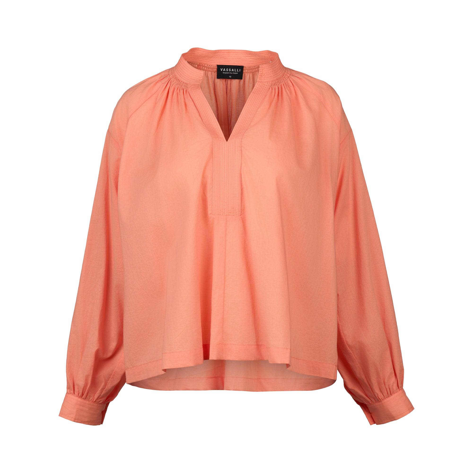 The Vassalli Placket Shirt in Apricot is a loose-fitting, long-sleeved cotton top with a V-neckline, gathered shoulders, and buttoned cuffs, shown on a plain white background.