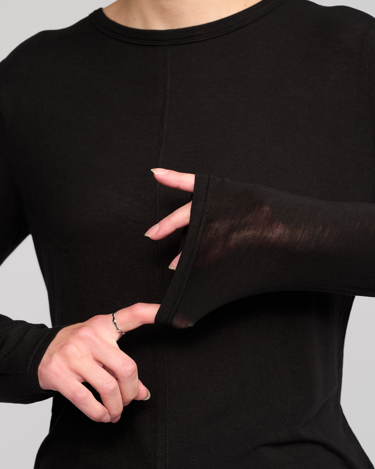 A model in the Vassalli Layer Top - Black highlights its smart design by slipping her thumb through the sleeve’s thumb hole, gently pulling the fabric to showcase this stylish wardrobe essential.