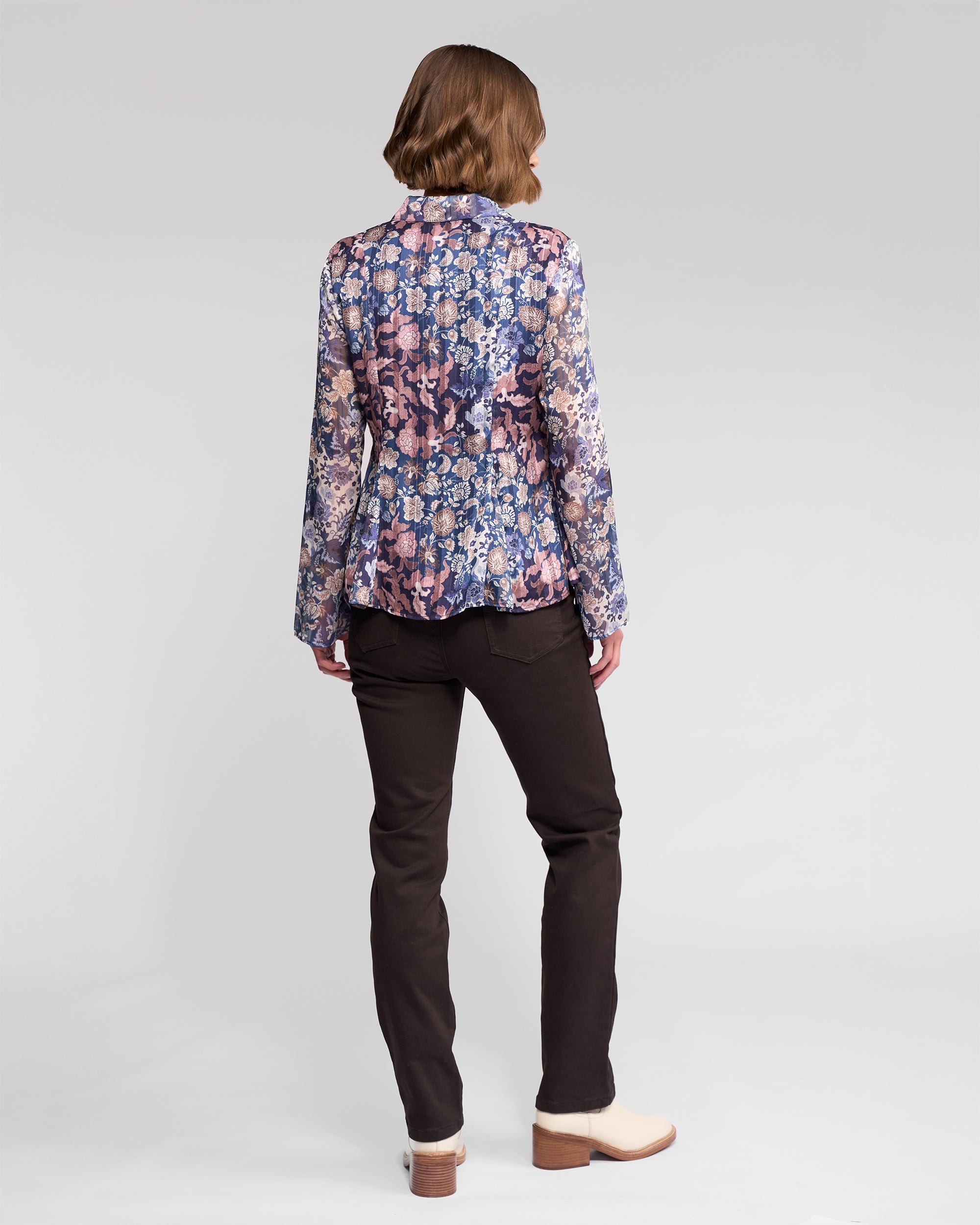 A person with short brown hair, seen from behind, wears the Vassalli Valley Shirt - Rhea with long sleeves, dark pants, and light low-heeled shoes, standing against a plain light background.