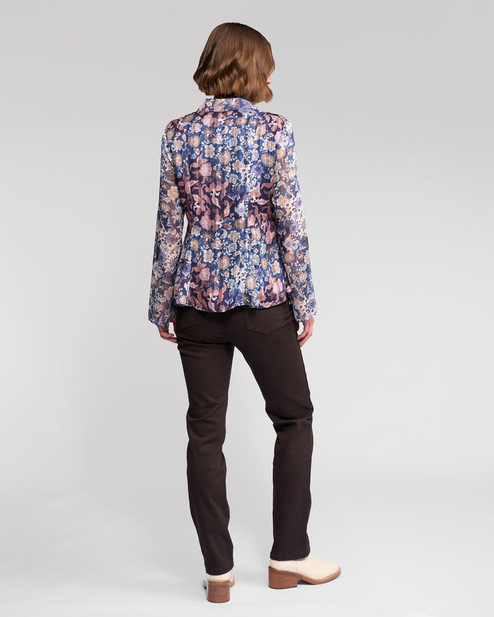 A person with short brown hair, seen from behind, wears the Vassalli Valley Shirt - Rhea with long sleeves, dark pants, and light low-heeled shoes, standing against a plain light background.