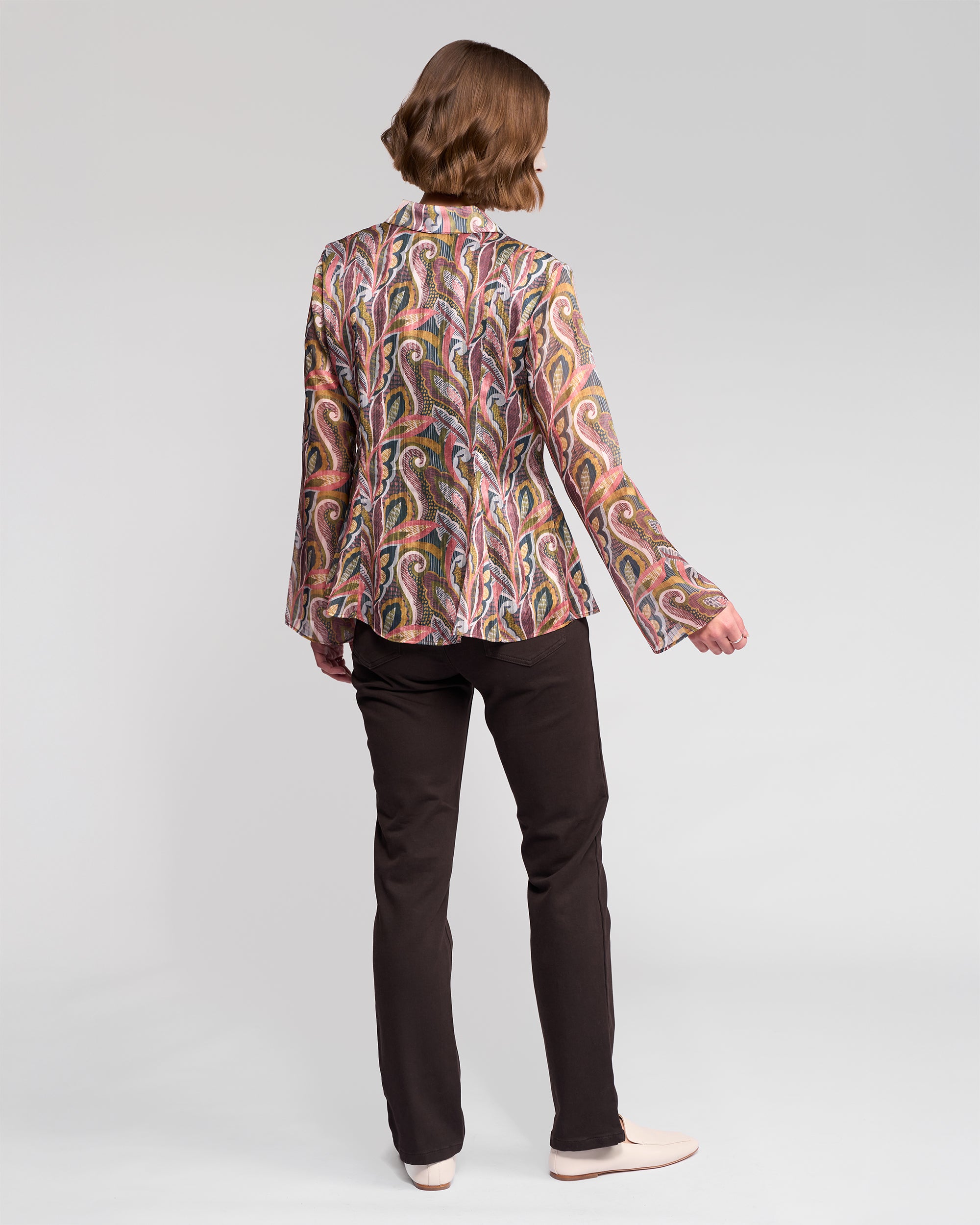A person with short brown hair, wearing the Vassalli Valley Shirt in Sable, black pants, and light shoes, stands facing away against a plain light background.