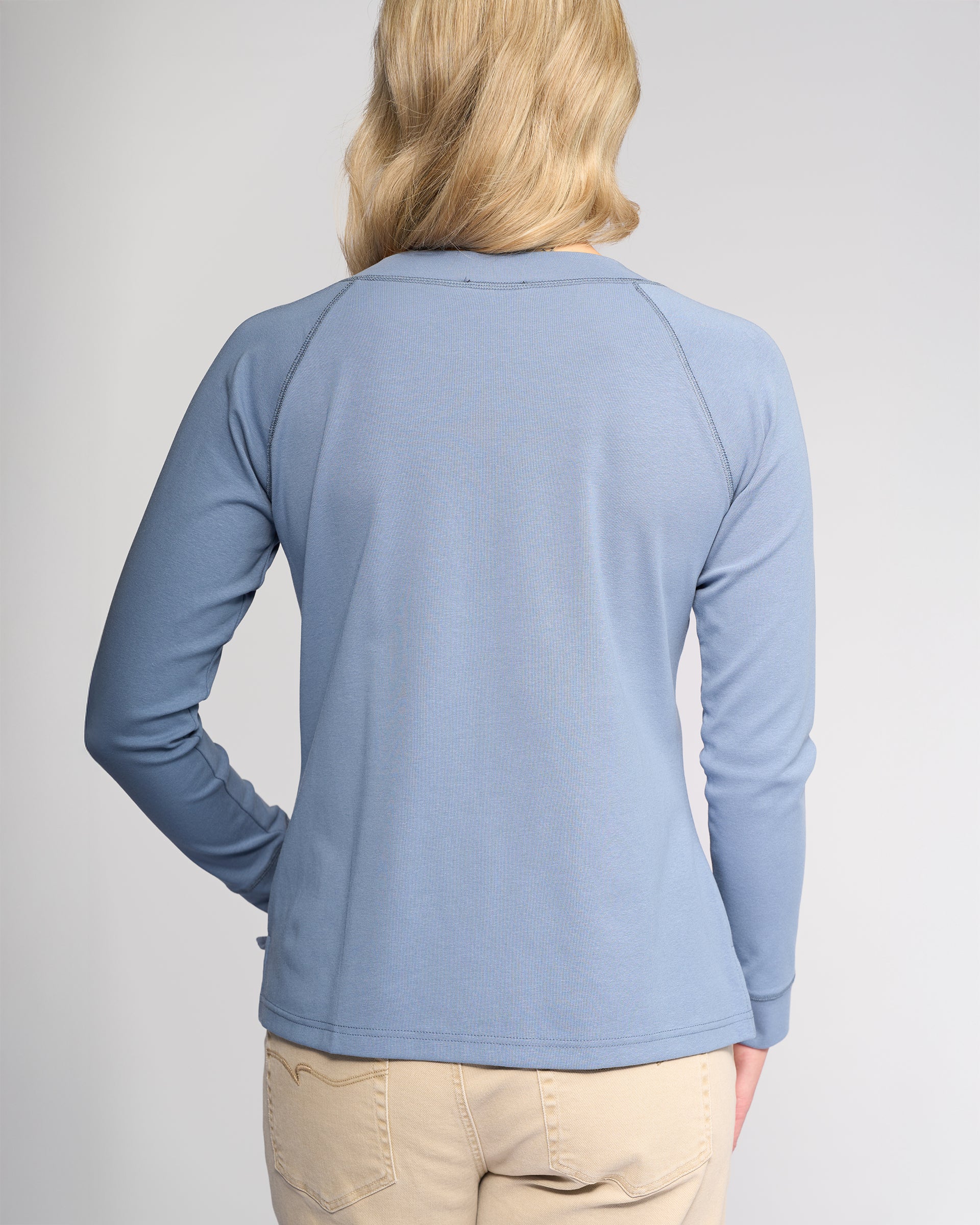 A person with blonde hair is facing away, wearing the Vassalli Key Top in denim blue and light beige pants, against a plain light background.