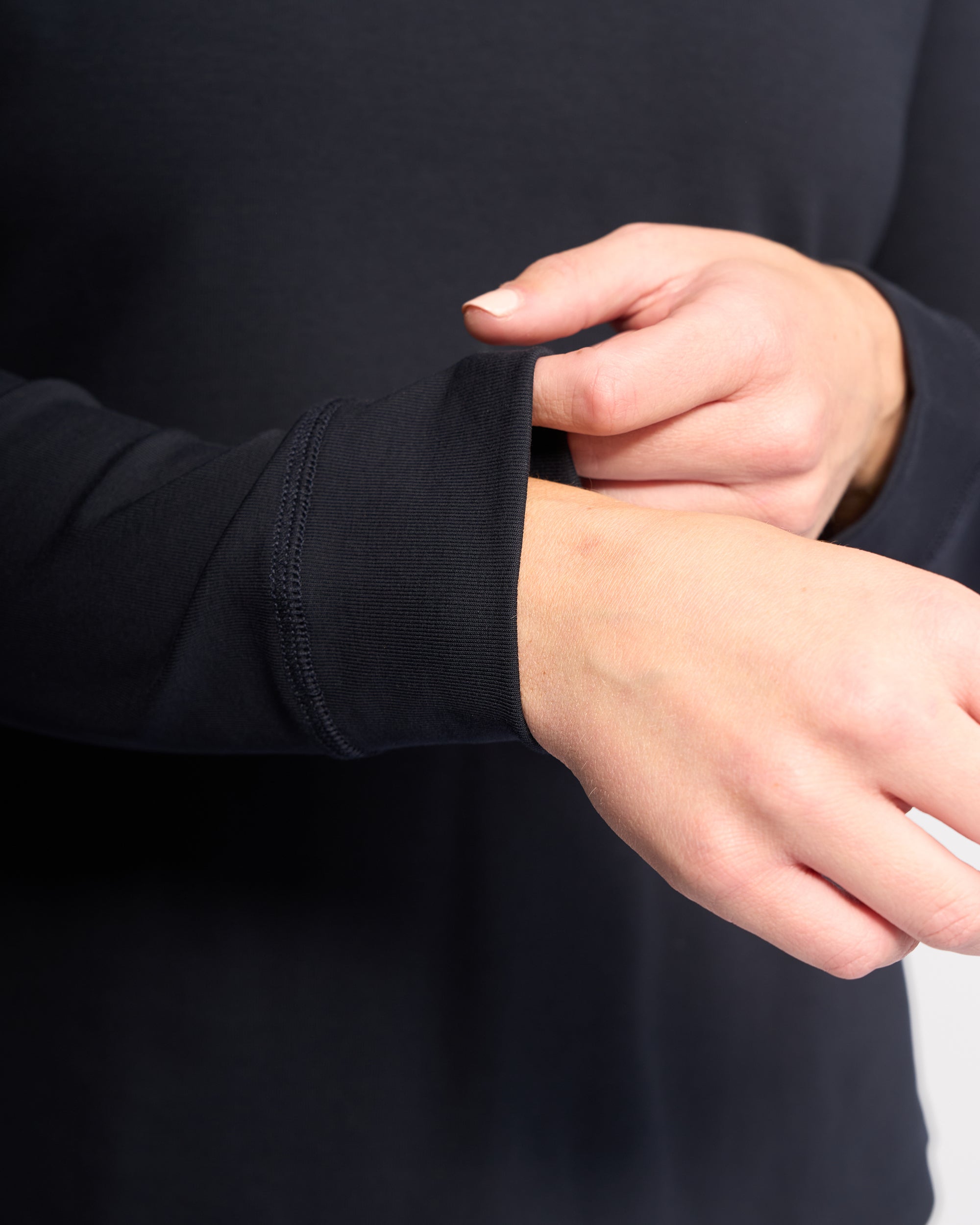 A close-up of hands adjusting the sleeve of the Vassalli Key Top - Ink, a black stretch cotton long-sleeve, with part of the torso visible against a plain background for a relaxed, casual look.