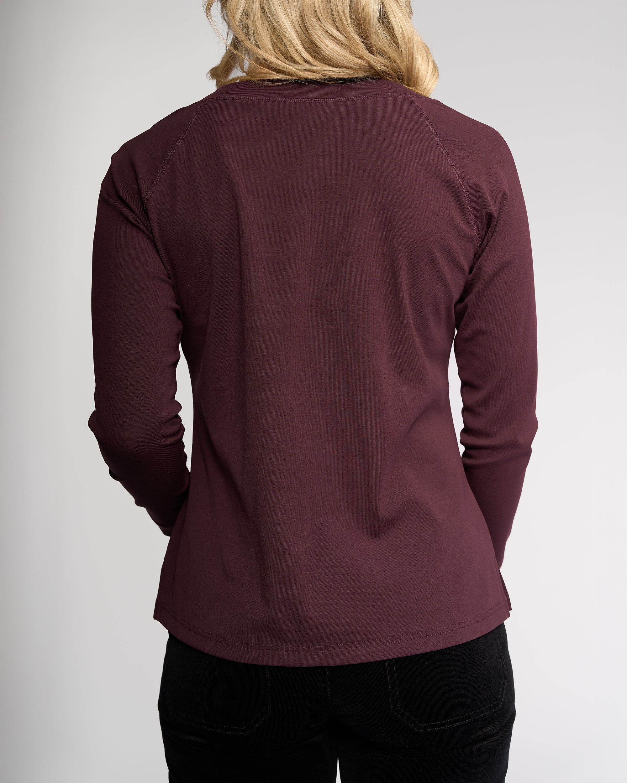A person with blonde hair is shown from the back, wearing the Vassalli Key Top - Pinot and black pants against a plain, light background.