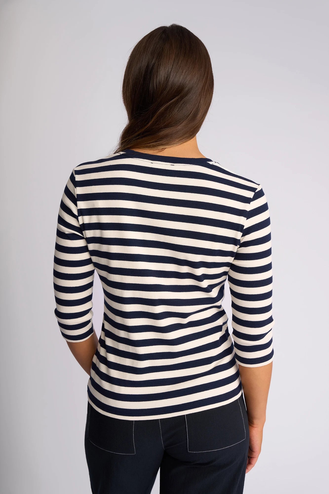 A person with brown hair, seen from behind, wears the Vassalli Callie Top in Ink/Cream—featuring three-quarter sleeves and ribbed knit stripes—paired with dark pants.