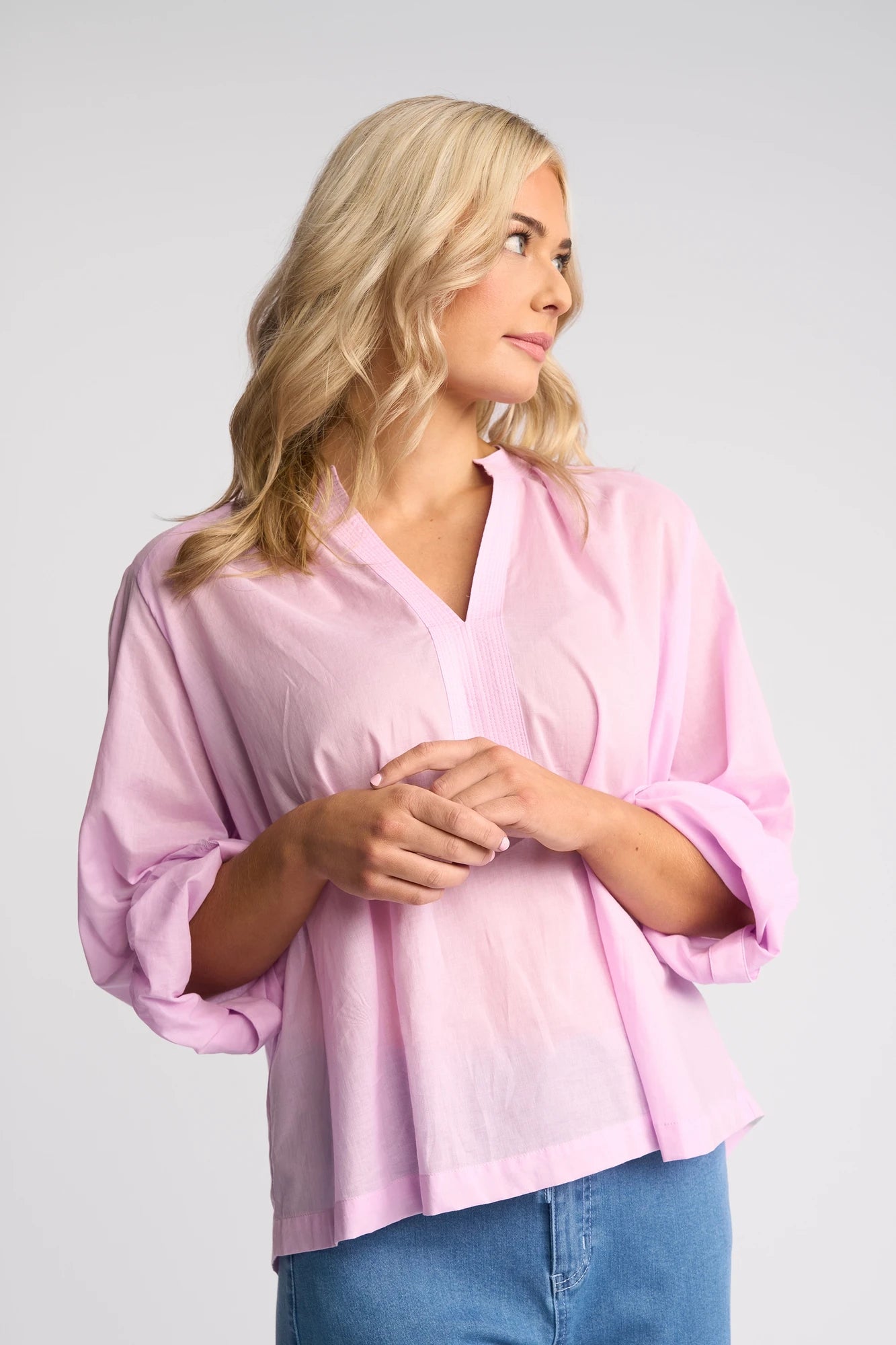 A woman with blonde hair wearing the Vassalli Lily Shirt in Light Purple and blue jeans stands against a plain background, looking to her left with a neutral expression.