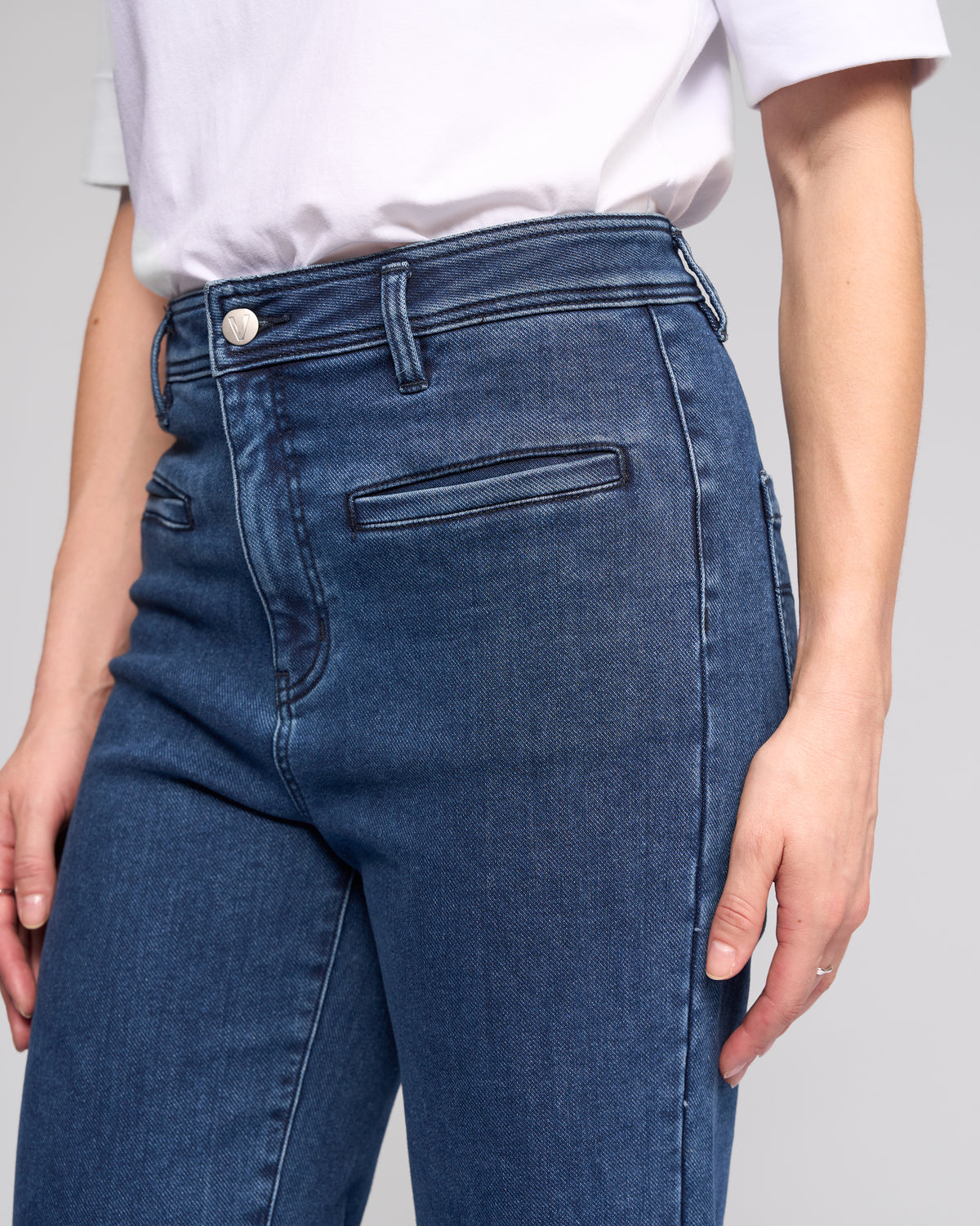 Wearing Vassalli’s Peace Jean in Brushed Indigo, this person sports high-waisted, wide-leg denim with a white short-sleeve shirt, their hand by their side and the look pictured from the torso down for a relaxed silhouette.