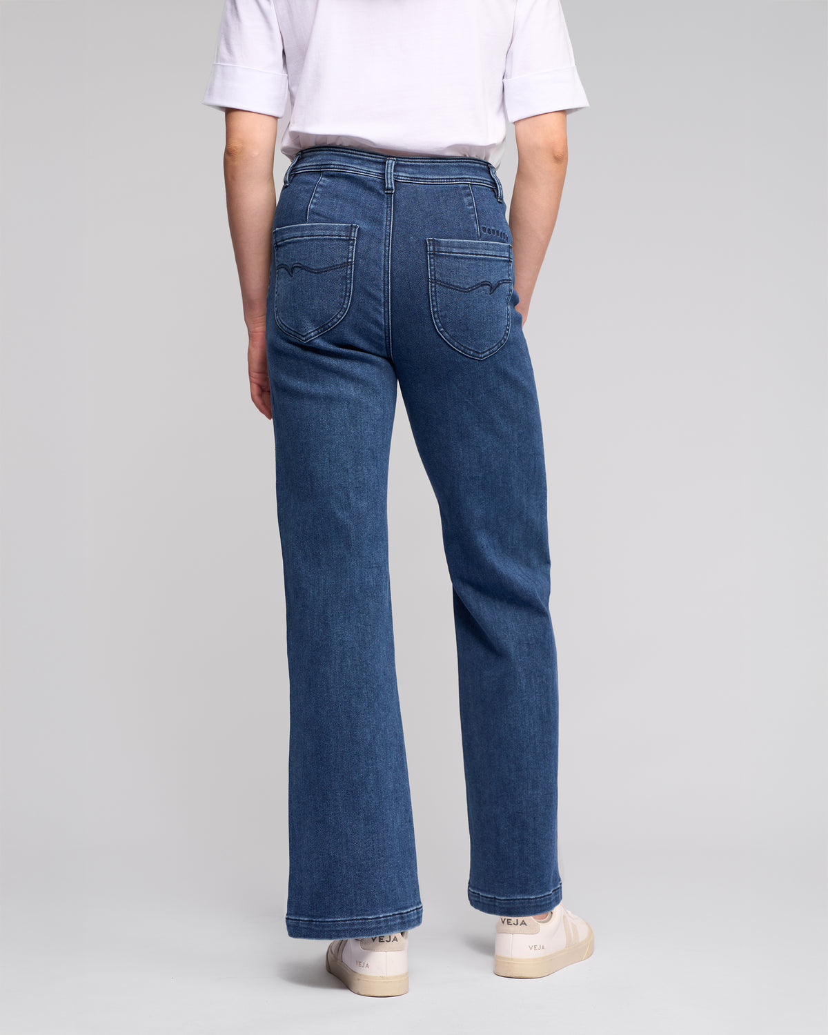 A person wearing Vassalli's Peace Jean - Brushed Indigo stands facing away, highlighting the relaxed silhouette of the high-waisted, wide-leg denim against a plain light background.