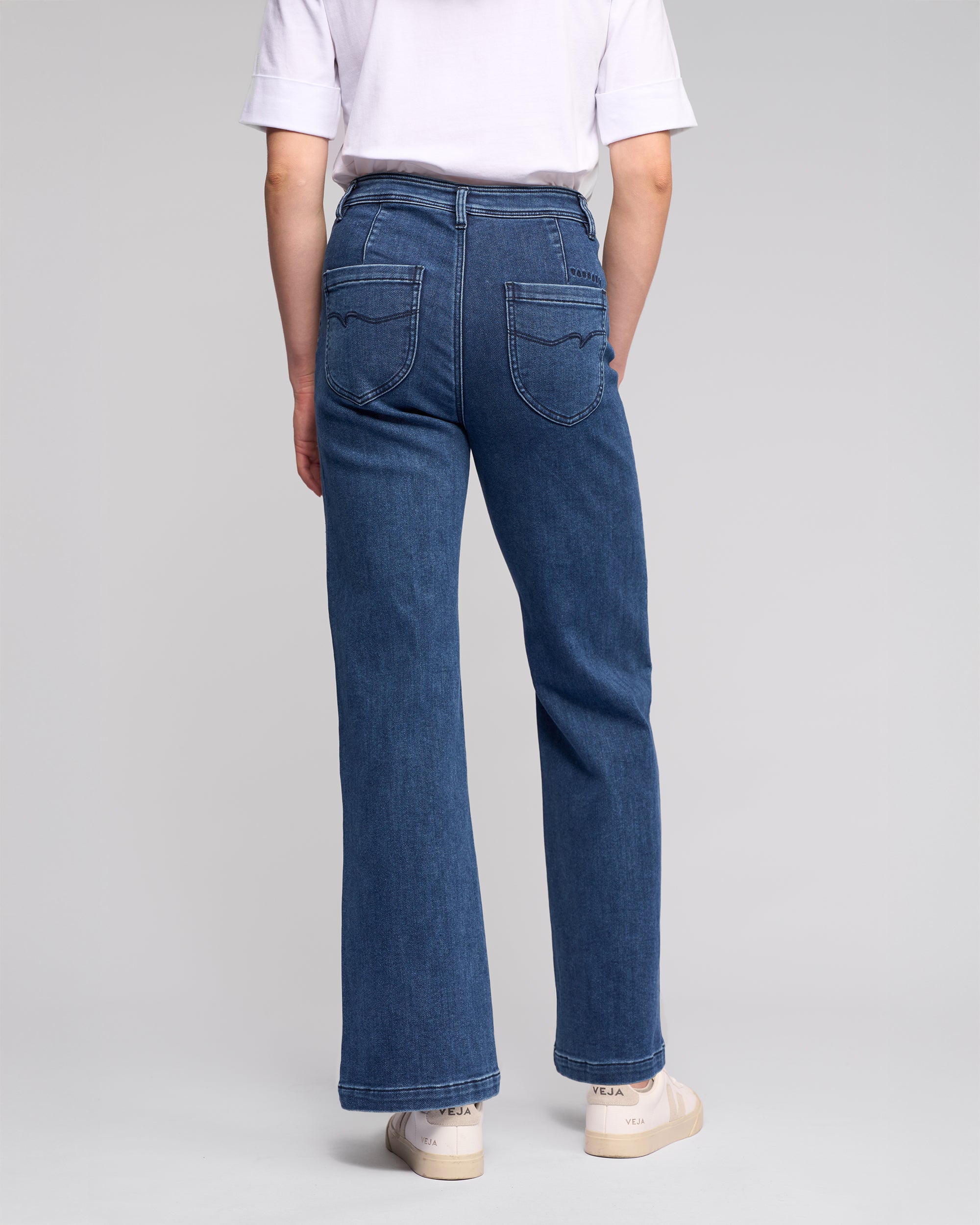 A person wearing Vassalli's Peace Jean - Brushed Indigo stands facing away, highlighting the relaxed silhouette of the high-waisted, wide-leg denim against a plain light background.