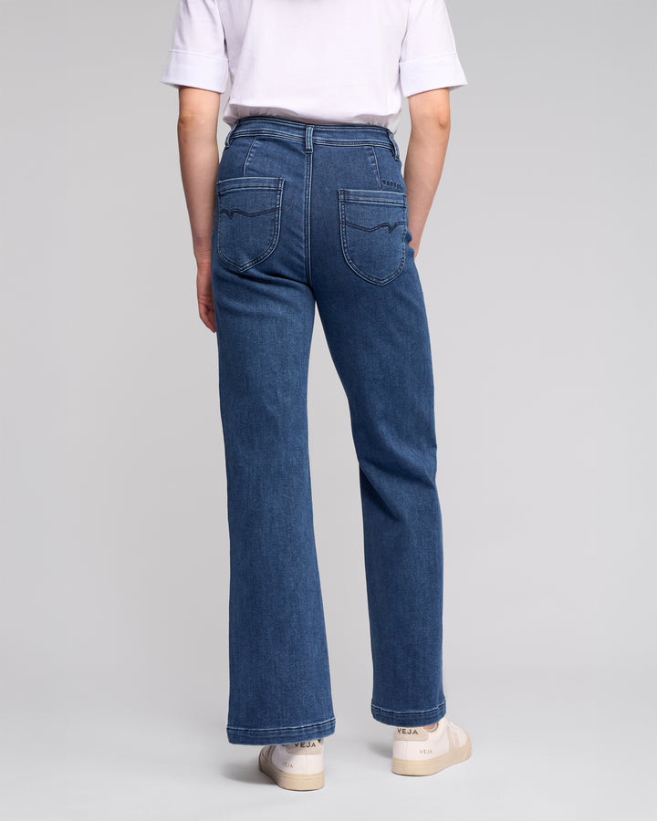 A person wearing Vassalli's Peace Jean - Brushed Indigo stands facing away, highlighting the relaxed silhouette of the high-waisted, wide-leg denim against a plain light background.