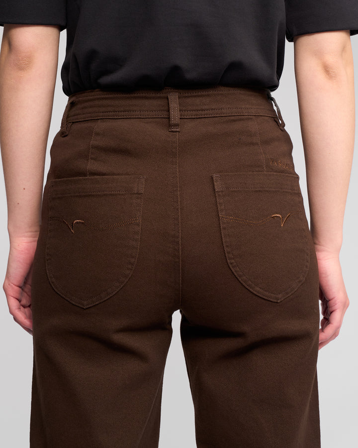 Someone wearing the Vassalli Peace Jean - Chocolate, high-waisted with back pockets, and a black shirt, shown from the waist down and viewed from behind.