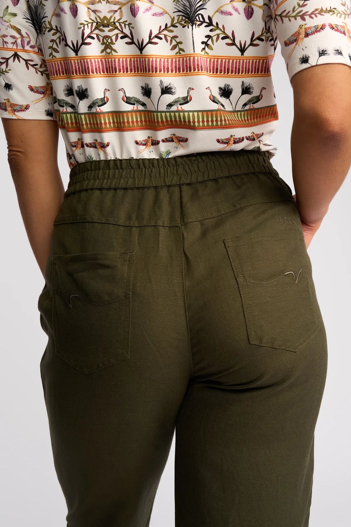 A person wearing Vassalli Oxford Pant in Khaki and a patterned shirt with birds and plants. The photo shows their back from waist to mid-thigh.