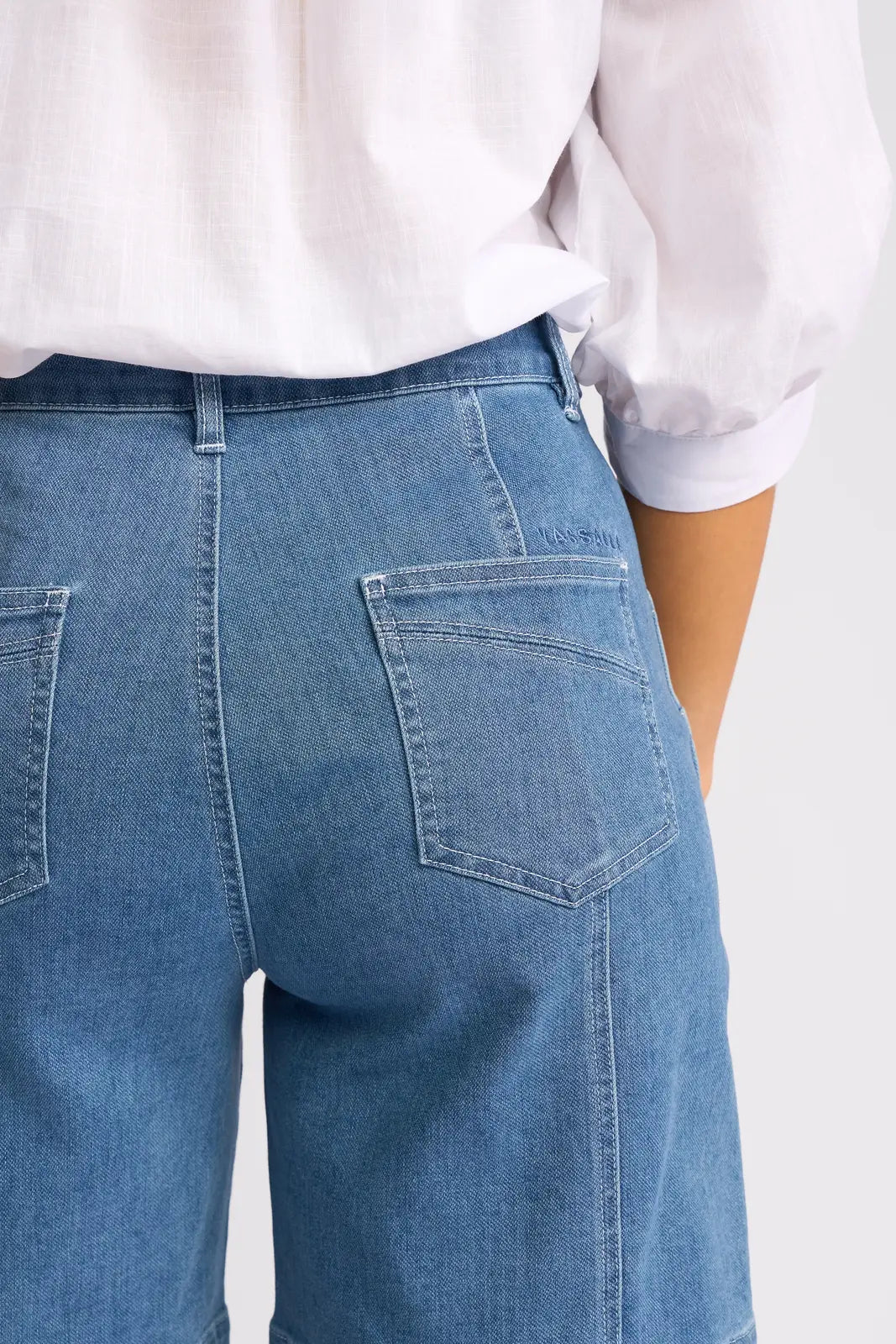 A person shown from the back wearing the Vassalli Raven Short in Blue Hue Denim, styled with a white long-sleeve shirt—the classic summer look is highlighted by the high-waisted fit and visible back pockets.