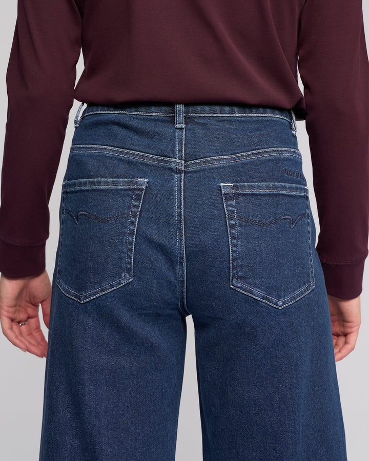A person is shown from the back wearing a long-sleeve burgundy top and Vassalli Alley Jean - Dark Blue, featuring a high-waisted, wide-leg silhouette, ankle length, and two back pockets with decorative stitching.