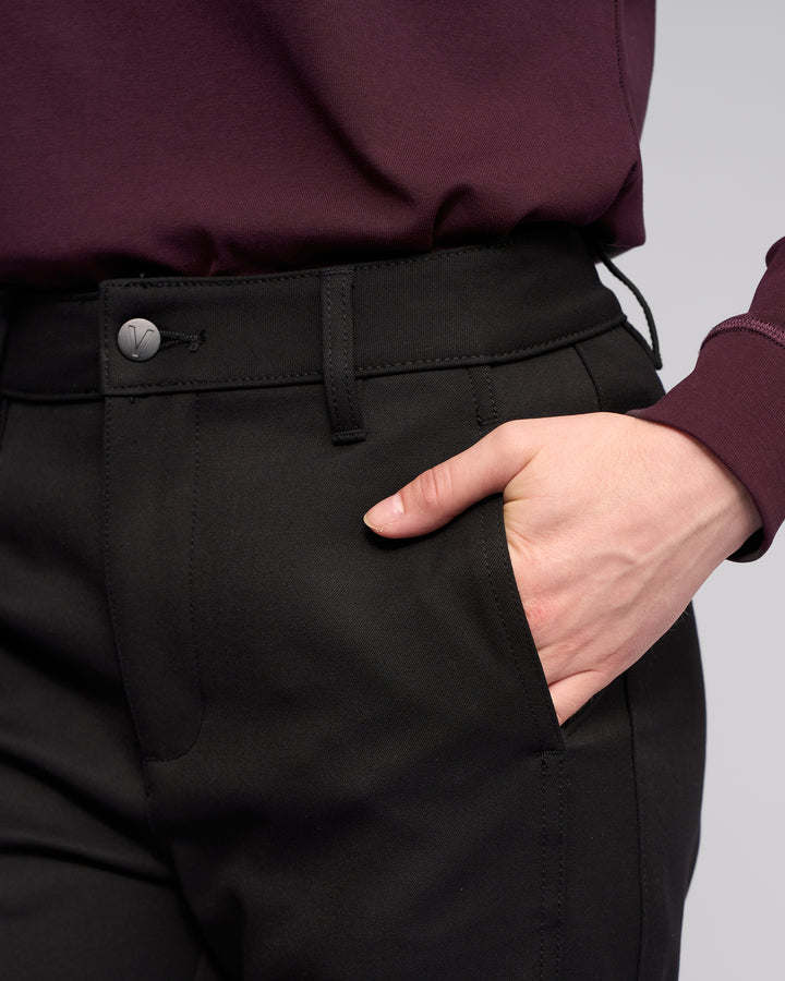 Model wears Vassalli’s Neve Pant in black with a burgundy long-sleeve top, right hand in pocket. The photo is cropped to highlight the waist and hand, without showing the model’s face.