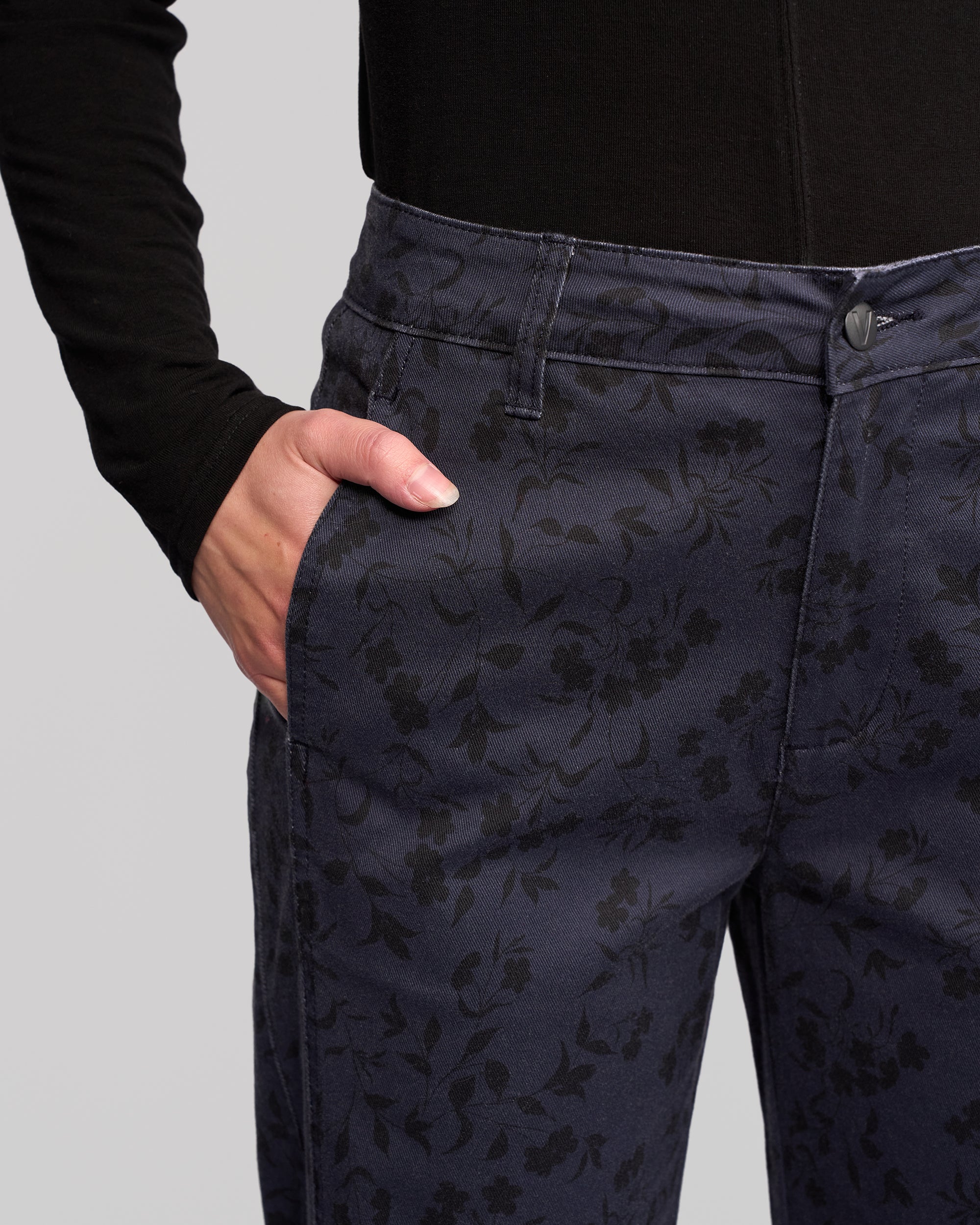 A person models the Vassalli Neve Pant - Noir with a black long-sleeve top, one hand in their pocket, highlighting the sleek straight-leg ankle-grazer denim in a close-up of the outfit and hand.