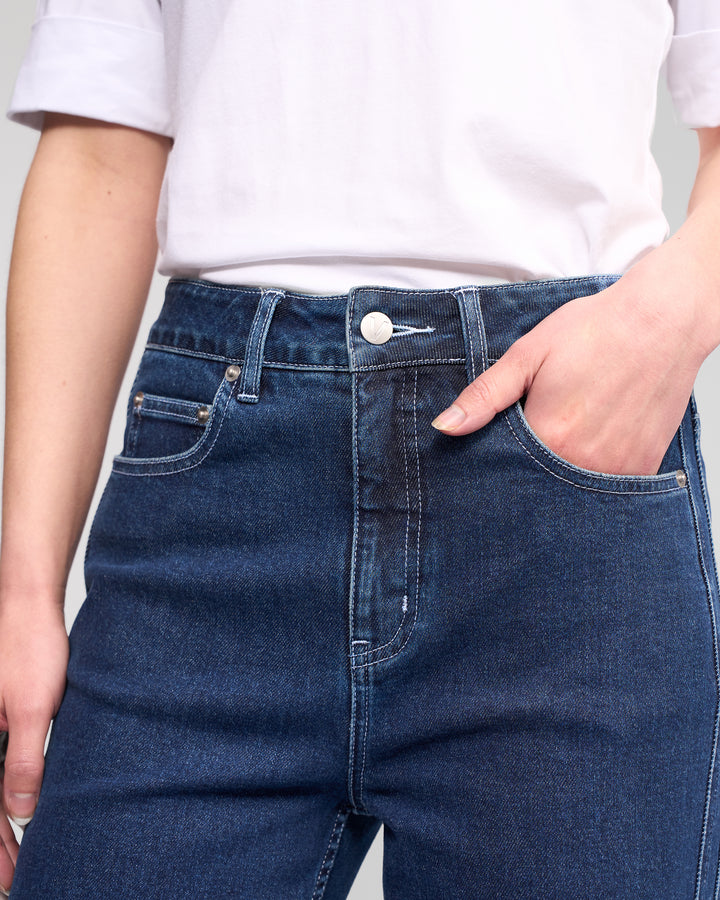 A person wearing a white t-shirt and Vassalli’s Wren Jean - Dark Blue, high-waisted with wide legs, with one hand in a front pocket. The photo is cropped to show the torso and upper legs.