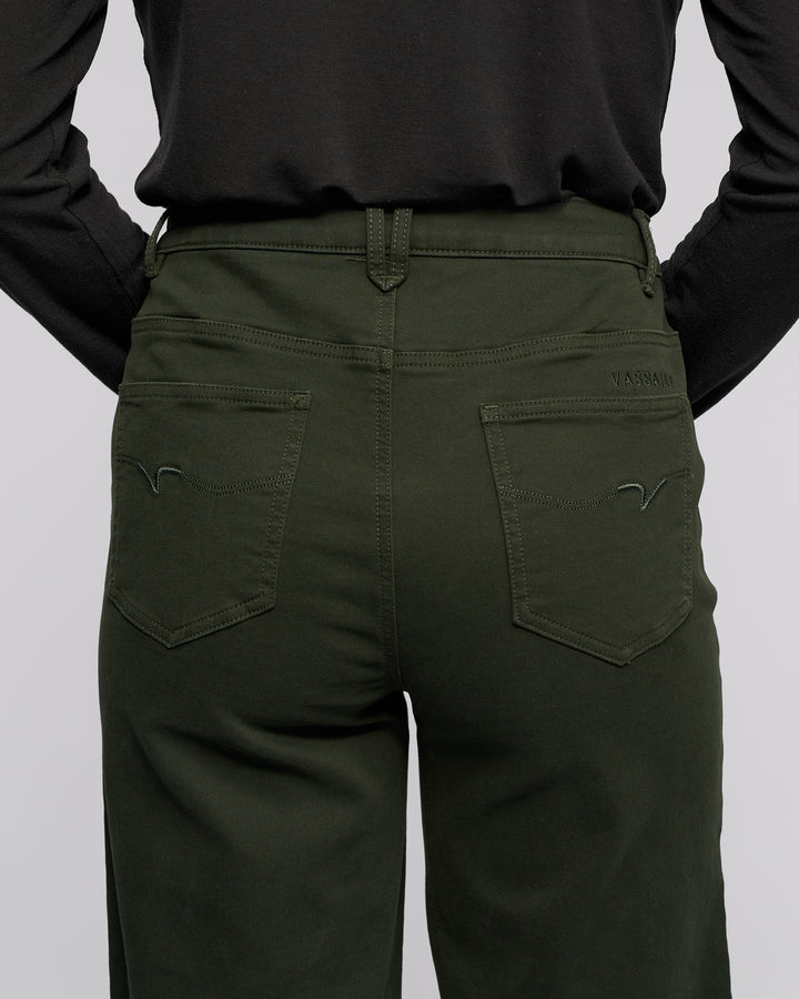 A person shown from the back wearing Vassalli’s Solo Pant in Forest—a wide-leg cotton tencel jean with two back pockets featuring stitched designs and a small brand label above the right pocket—and a black long-sleeve shirt.
