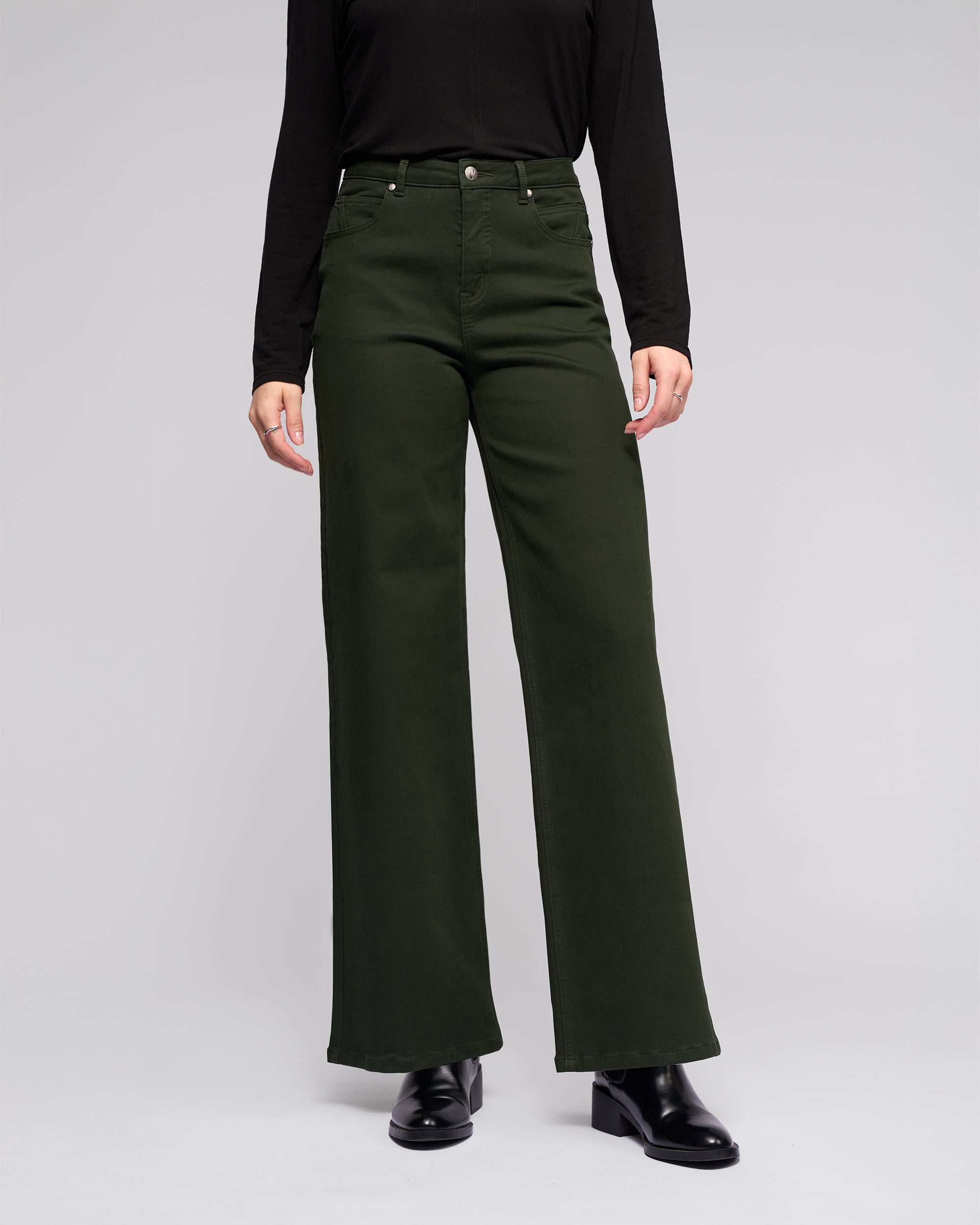 A person models the Vassalli Solo Pant - Forest, a high-waisted wide-leg style, with a black long-sleeve top and black shoes against a plain light gray background.