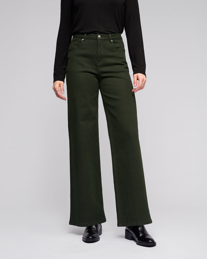A person models the Vassalli Solo Pant - Forest, a high-waisted wide-leg style, with a black long-sleeve top and black shoes against a plain light gray background.
