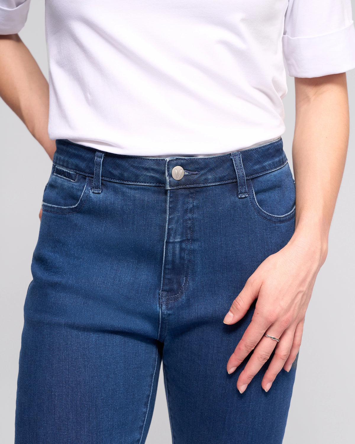 Wearing a white short-sleeve shirt and Vassalli Radio Jean - Blue Denim, a person stands with one hand on their hip and the other by their side.