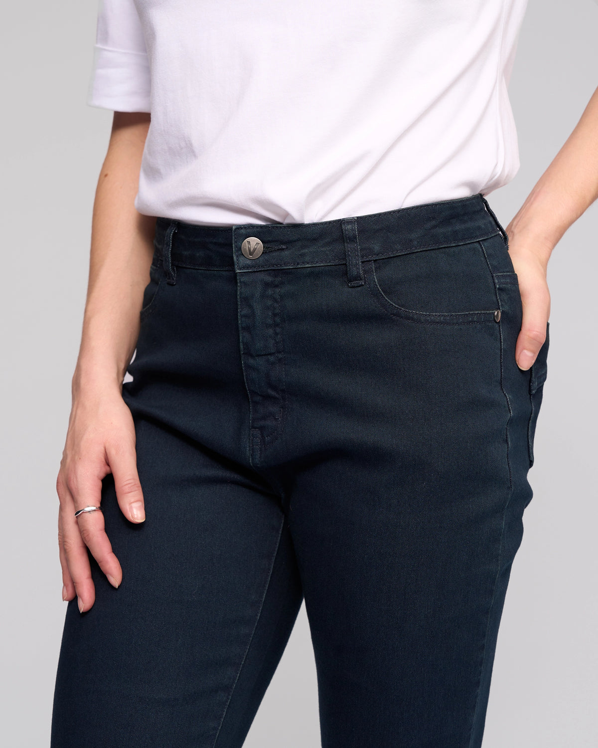 A person models the Vassalli Radio Jean - Indigo Denim, showcasing its straight-leg style. They're in a white short-sleeve shirt, with one hand in their pocket and the other by their side; photo is cropped from shoulders to mid-thigh.