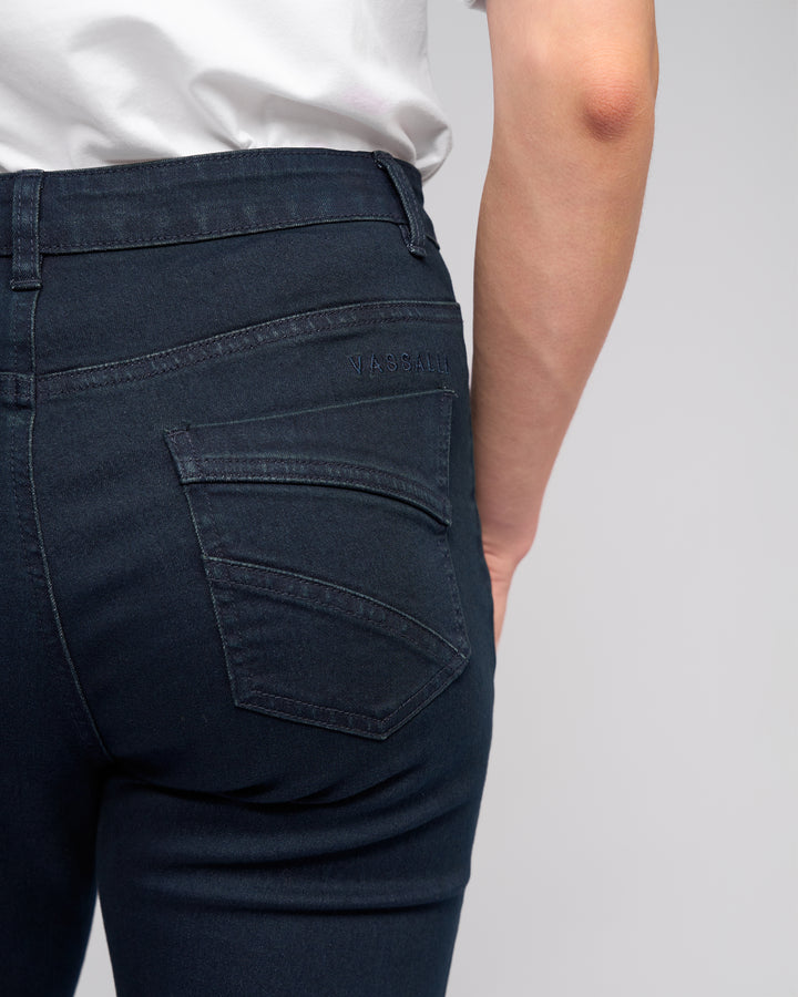 Close-up view of a person wearing Vassalli Radio Jean - Indigo Denim, showcasing the straight-leg fit, visible stitching, and "VASSALLI" embroidered above the back pocket alongside a white shirt.