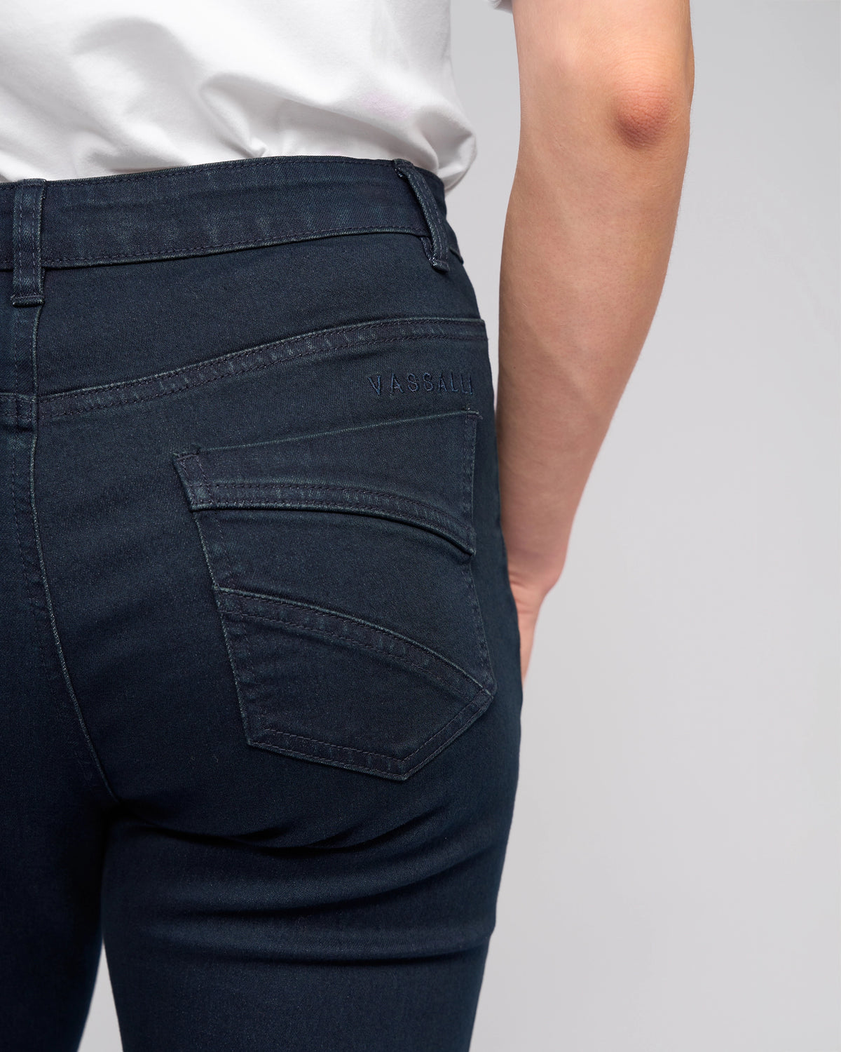 A person seen from behind wears the Vassalli Radio Jean in indigo denim, highlighting the waistband and back pocket details against a plain light background.
