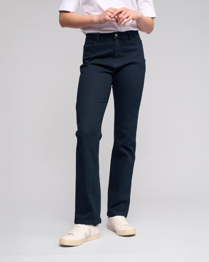 Person wearing a white t-shirt, Vassalli Radio Jean in indigo denim, and white sneakers, standing against a plain light background with hands clasped at waist.