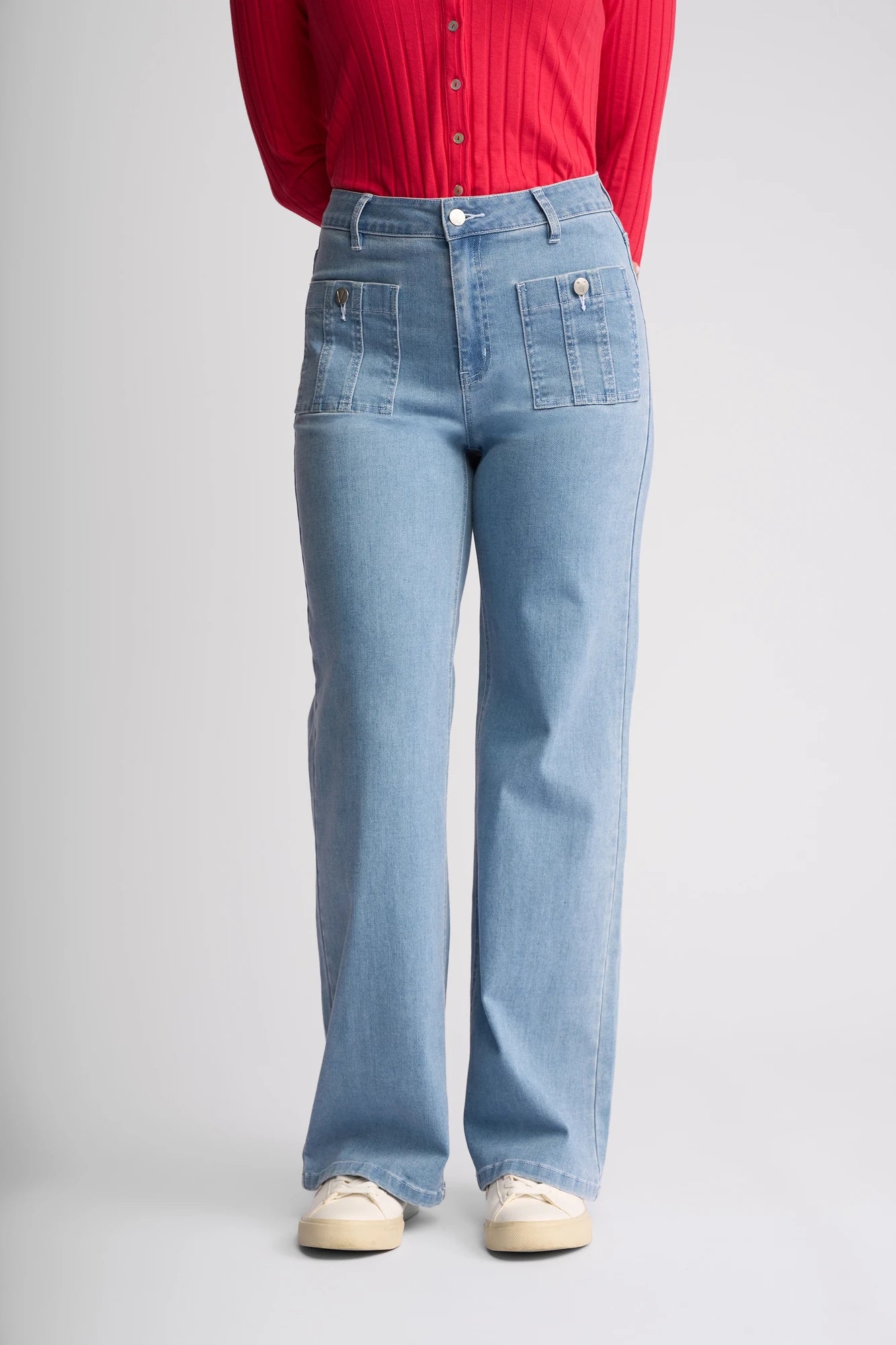 A person wearing the Vassalli Lottie Jean in Light Wash Denim, styled with a red ribbed long-sleeve top and cream sneakers, stands against a plain light background.
